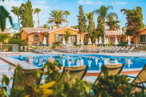 Zwembad van Suites & Villas by Dunas met ligbedden en witte parasols, omgeven door palmbomen en groen.